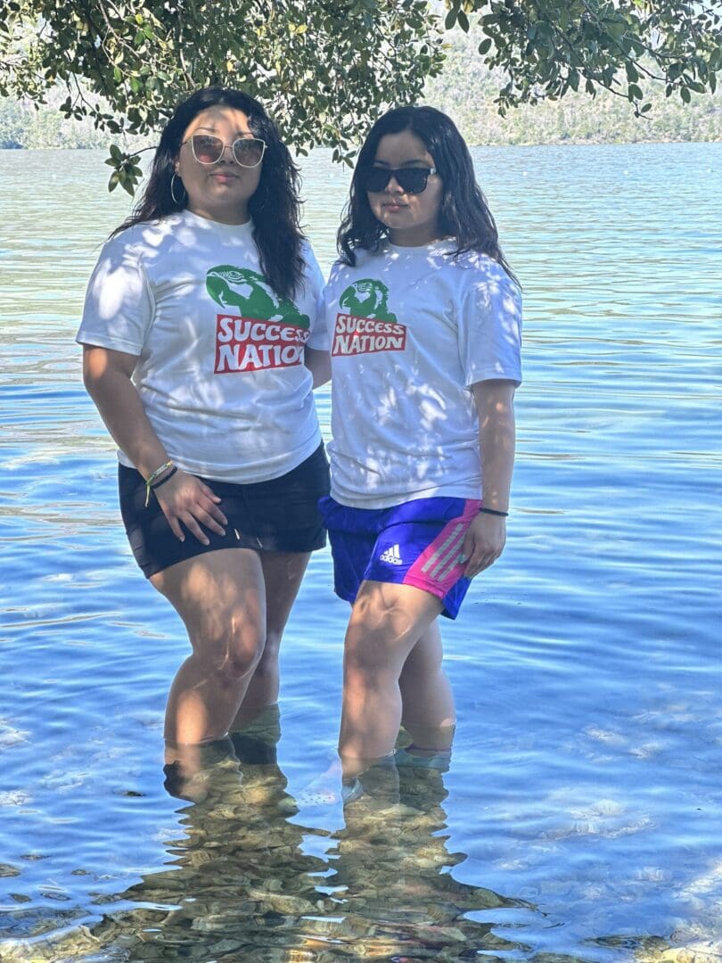 Two women standing in the water wearing white shirts.